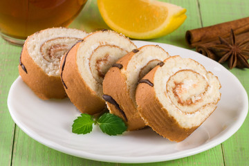 Biscuit swiss roll with a cup of tea on green wooden background