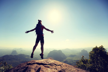 cheering successful young woman hiker jumping on mountain peak