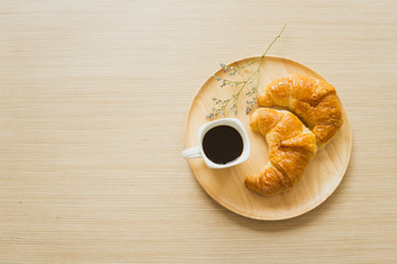 espresso coffee in white modern mug  with fresh bake croissant and flower on wooden plate on wooden table with morning light