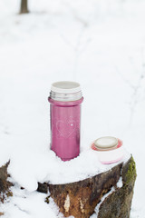 Nice warm thermos bottle with tea or coffee outdoors on the snow on a background of a winter landscape. Cozy winter still life. Relax after long winter walk.