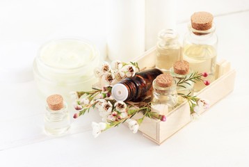 Bottles of essential aroma oil in wooden container with delicate flowers, white table copyspace. Botanical beauty treatment. 