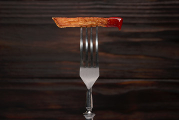 French fries and ketchup on a fork with wooden background.