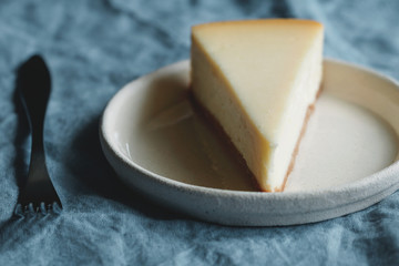 Selective focus of front piece of cheesecake on a light plate on a blue background