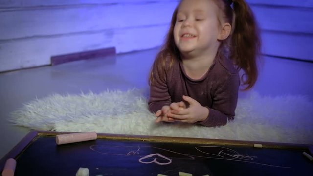 Little girl is drawing with chalk on a blackboard