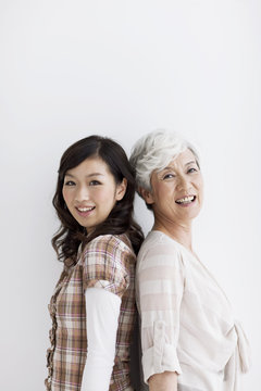 Portrait of mature woman and young woman standing back to back, smiling, white background