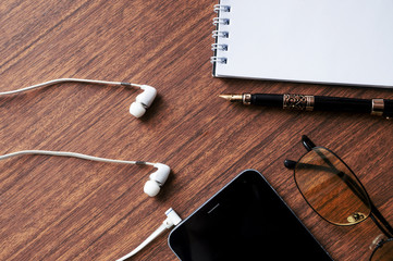 View of business have a phone, notebook, Goggles, headphones, pen and mobile phone with on wooden red background