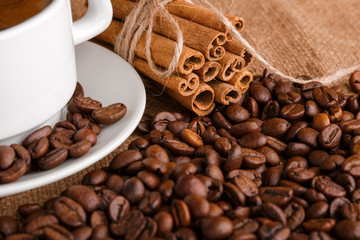 Coffee beans and cinnamon on a background of burlap. Roasted coffee beans background close up. Coffee beans pile from top with copy space for text. Seasoning. Spice. Cinnamon. Badian. Coffee house.
