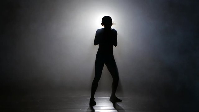 Champion boxer in the smoke sends kicks. Silhouette. Lights rear. Black background