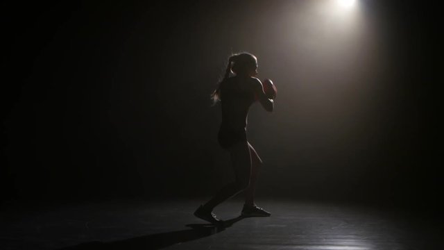 Champion boxer sends the punches. Silhouette. Lights rear. Black background. Side view
