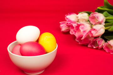 Obraz na płótnie Canvas easter background, colorful eggs in ceramic bowl and roses bouquet over red paper