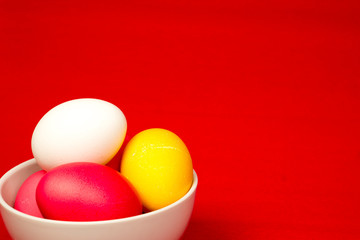easter background, colorful eggs in ceramic bowl over red paper