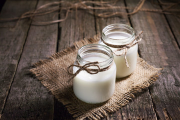 Fresh cow milk or cream in glass bottles, rustic style, vintage wood background