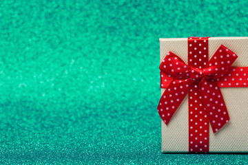 Gift box with red bow on sparkling green background. Bright and festive.