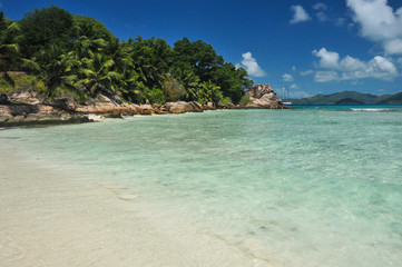 Granite stones on tropical white-sand beach next to turquoise water