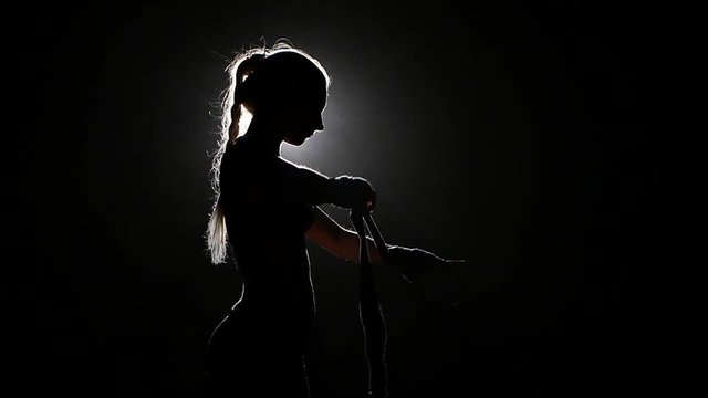 Boxer shakes special bandages on his hands. Silhouette. Black background . Side view. Close up. Slow motion