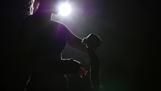 Boxer pulls in his arms protective bandages. Silhouette. Black background . Side view. Close up. Slow motion