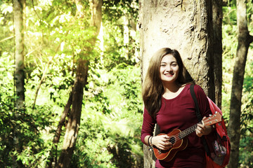 Young Beautiful Asian Woman is sitting and playing guitar,Woman playing acoustic guitar in central park Cute young adult girl sit big forest.