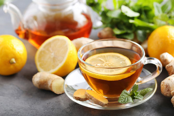 Cup of tea with ginger root and lemon on grey wooden table