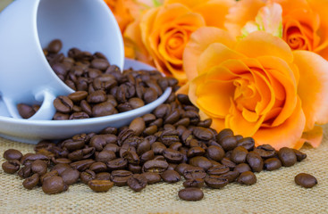 An espresso cup, roses and roasted coffee beans lie on a table