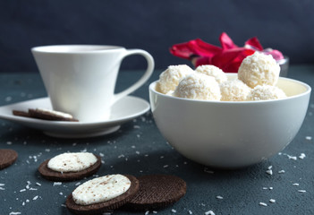 Sweets round white with coconut shavings in a white bowl and tea in a cup on a dark blue background
