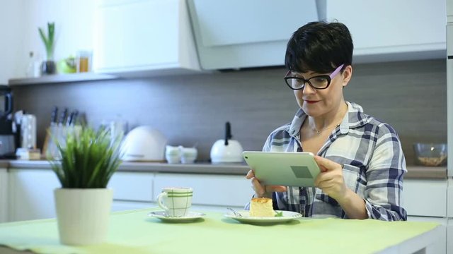 Attractive woman doing selfies on tablet while sitting by the table in the kitchen
