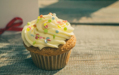 Soft cupcake with giftcard on wooden vintage background. Home-made pastries. Soft toning