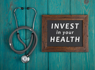 Blackboard with text "Invest in your health" and stethoscope on blue wooden background