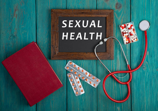 Blackboard with text "Sexual Health", book, pills and stethoscope on blue wooden background