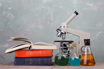 Obraz na płótnie Canvas chemical flasks, books and microscope on the desk on green background