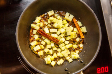 Sliced apples fried with cinnamon sticks in the sugar in the pan.