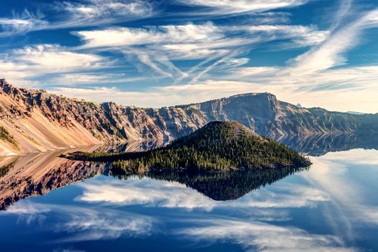 A perfect reflection of Wizard island with some amazing clouds in motion at Crater lake, just after sunrise. Crater lake National Park, Oregon.
