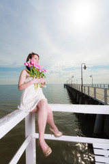 Woman holding bouquet of flowers sitting on pier