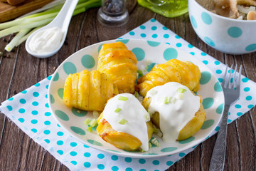 Baked potato with cheese served with cream sauce and greens on a wooden table in a rustic style.