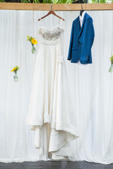 wedding dress of bride and groom hanging on white wall