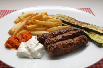 Cevapcici mit Pommes frites, Zucchini, Ajvar und Tzatziki.