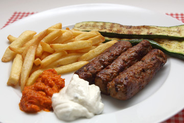 Cevapcici mit Pommes frites, Zucchini, Ajvar und Tzatziki.