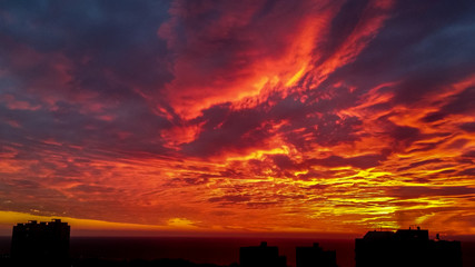 Dramatic bloody red orange colored sky sunset above silhouette of cityscape buildings Haifa city...