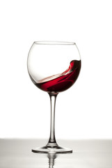 Red wine splashes out of a glass making waves in the glass