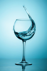 Water or alcohol splashes out of a glass making waves in the glass
