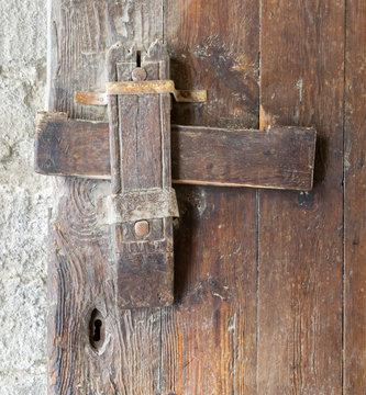 Front view closeup of a wooden aged latch, and keyhole over a wooden opened door