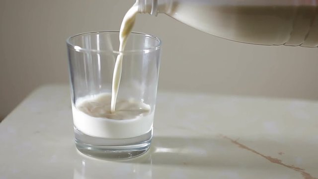 Fresh milk, it is poured in a glass. The roller doesn't contain the advertizing text and emblems. The transparent mug and a bottle of white color are used. An indistinct background with studinny light