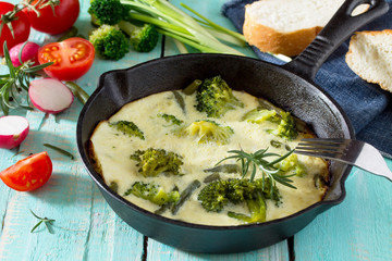 Scrambled eggs with broccoli and green beans with fresh different vegetables on a wooden table. The...