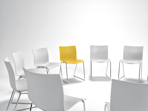 Single yellow chair in a circle of white