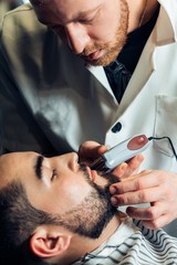portrait of handsome man with beard in barbershop. barber working with electric razor