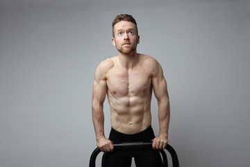 Shirtless muscular athlete doing push-up on push up bars. White background.