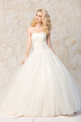Fototapeta na wymiar a gorgeous smiling blonde bride with curly hair in a white wedding dress to the full-length on a light background. beautiful young model with bridal hairstyle and makeup in a white magnificent dress.
