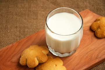 A glass of milk with cookies on a wooden board on a background sacking