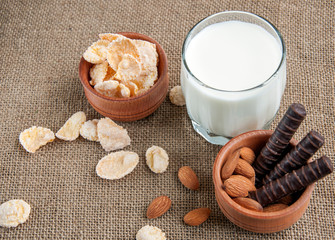 A glass of milk with almond nuts, corn flakes, chocolates,  on sacking background
