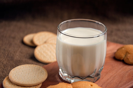 A glass of milk with cookies on a wooden board on a background sacking