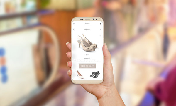 Woman buy shoes online with mobile phone app. Purchase of modern dress shoes. Buy now button on mobile app. Shopping mall in background.